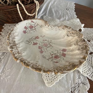 May include: A white porcelain serving dish with a gold rim and floral pattern. The dish has a scalloped edge and is decorated with pink and green flowers.