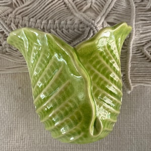 May include: A green ceramic vase shaped like a leaf. The vase has a glossy finish and a textured surface.