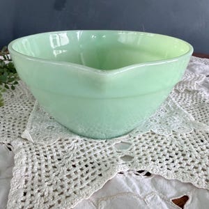 May include: A white ceramic mug with a black handle and the text "But First, Coffee" in a black, handwritten-style font. The mug is on a white surface.