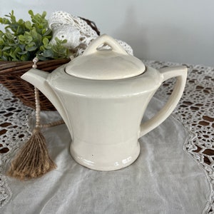 May include: A white ceramic teapot with a lid and a handle. The teapot has a simple, elegant design.