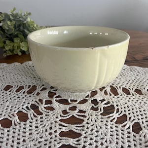 May include: A pale yellow ceramic bowl with a fluted design. The bowl is sitting on a white crocheted doily.