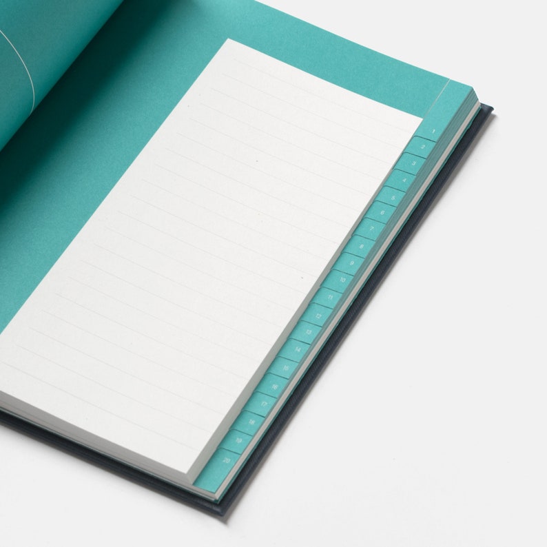May include: An open teal notebook with a white lined page and a teal index tab along the edge. The index tab has numbers from 1 to 20 printed on it.