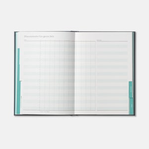 May include: An open, blank, blue and white planner with the text "Pflanzenkalender f&uuml;rs ganze Jahr" at the top of the left page. The planner has a grid layout with lines for dates and notes.