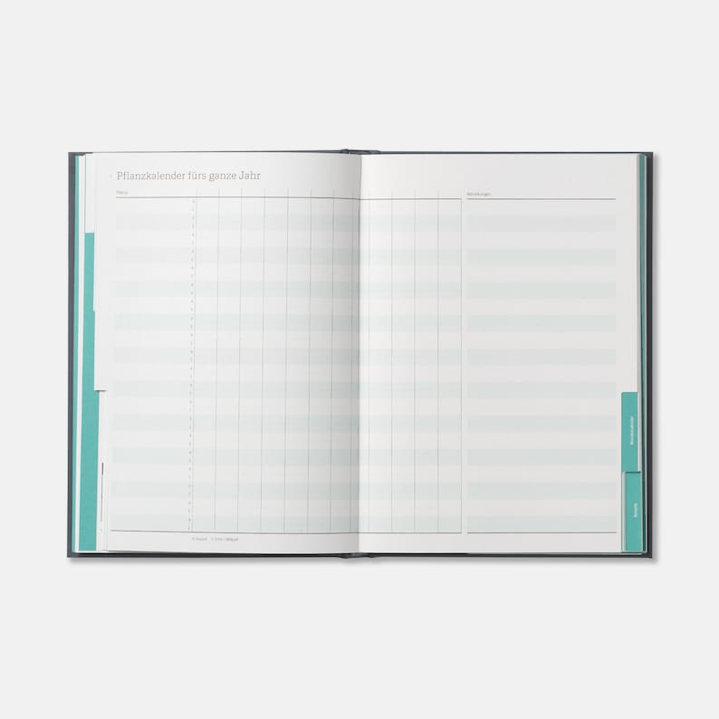 May include: An open, blank, blue and white planner with the text "Pflanzenkalender f&uuml;rs ganze Jahr" at the top of the left page. The planner has a grid layout with lines for dates and notes.