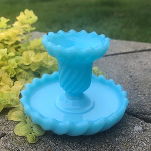 Puede incluir: Un plato de vidrio azul claro para baratijas con un borde festoneado y un pedestal a juego. El plato tiene un diseño de espiral.