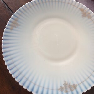 May include: A white ceramic plate with a blue and gold rim. The plate has a scalloped edge and a delicate floral design.
