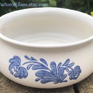 Könnte beinhalten: Eine weiße Keramikschüssel mit blauen Blumenmustern. Die Schüssel hat zwei Griffe an den Seiten und eine abgerundete Form.