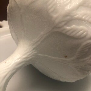 Puede incluir: Tazón blanco de vidrio de leche con pedestal y diseño floral en relieve. El tazón tiene un borde festoneado y una base con pie.