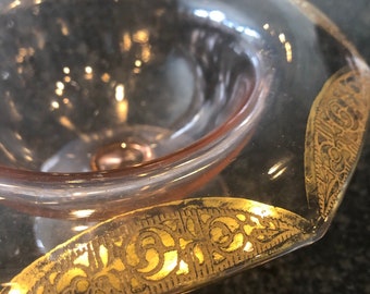 May include: A clear glass bowl with a pink rim and gold accents. The bowl has a decorative pattern around the rim.