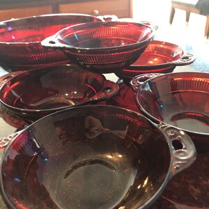Könnte beinhalten: Eine Sammlung von rubinroten Glasservierschalen. Die Schalen sind unterschiedlich groß und haben dekorative Griffe. Die größte Schale ist oval, die anderen sind rund. Die Schalen haben ein geripptes Design.