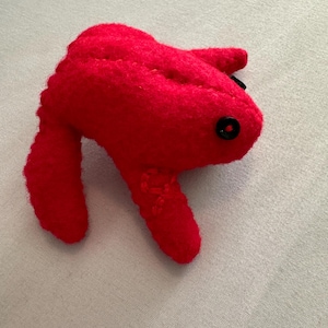 May include: A bright red plush toy shaped like a frog with black button eyes.
