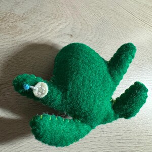 Puede incluir: Un juguete de cactus de fieltro verde con un botón blanco y una cuenta azul para los ojos.