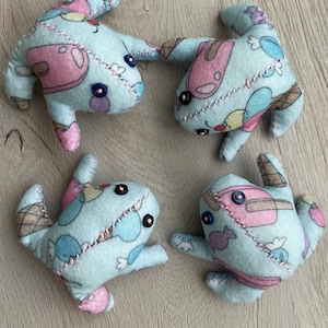 May include: Four handmade plush toys in a whimsical design. Each toy is a light blue color with pink, brown, and other pastel accents. The toys are stitched together with pink thread and feature button eyes.