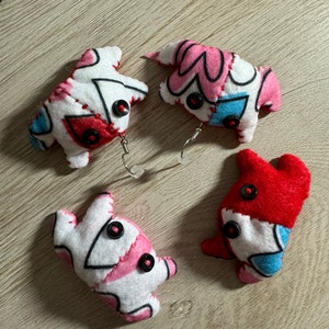 May include: Four handmade fabric earrings in the shape of a small animal. Each earring is made of different colored fabrics and has black buttons for eyes. The earrings are attached to silver hoops.