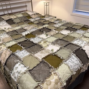 May include: A patchwork quilt in green, brown, and cream tones, covering a bed. The quilt has a diamond pattern with different fabric textures and floral designs. The bed has a metal frame.