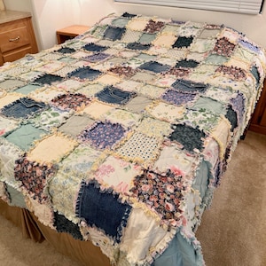 May include: A patchwork quilt made from various fabrics, including denim and floral patterns, covers a bed. The quilt displays a mix of colours, including blue, green, cream, and floral patterns. Wooden bedside tables are on either side of the bed.