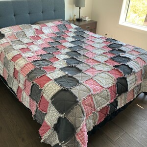 May include: A patchwork quilt with a checkered pattern in shades of pink, grey, and white. The quilt is made of various fabrics and has a frayed edge.