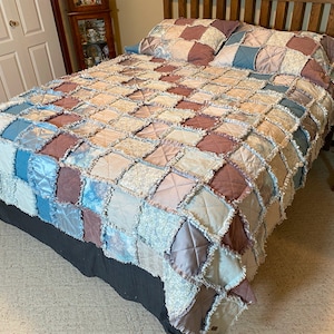 May include: A patchwork quilt featuring a mix of blue, pink and white colours and patterns. The quilt is made from squares of fabric sewn together to create a unique design. The quilt is displayed on a bed with a wooden headboard.