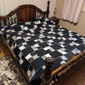 May include: A black and white patchwork quilt on a wooden bed frame with a headboard. The quilt is made of squares of different fabrics, some of which are frayed.