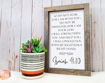 May include: A framed print with a white background and black text. The text reads "So do not fear, for I am with you; Do not be dismayed, for I am your God. I will strengthen you and help you; I will uphold you with my righteous right hand." The bottom of the print reads "Isaiah 41:10".