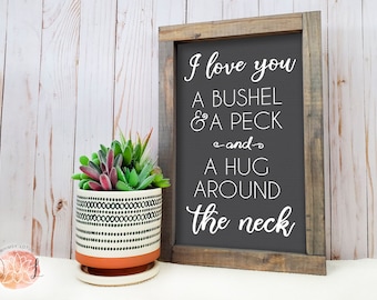 May include: A framed sign with a rustic wood frame and a dark gray background. The sign says "I love you a bushel & a peck -and- a hug around the neck".