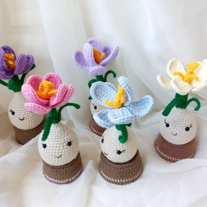 May include: Five crocheted flower pots with smiling faces. The flowers are in various colours, including purple, pink, blue, and white.