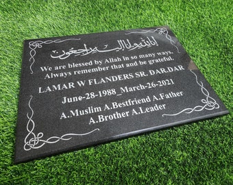 Puede incluir: Una placa conmemorativa rectangular de granito negro con texto grabado en blanco y adornos decorativos en las esquinas. La inscripción incluye caligrafía árabe, el nombre LAMAR W FLANDERS SR. DAR.DAR, fechas y varios títulos personales.