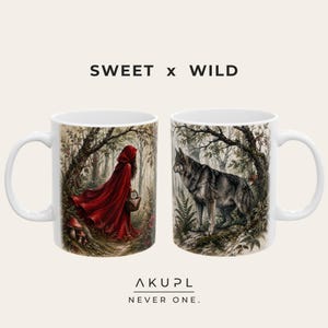 Può includere: Due tazze in ceramica bianca con una scena boschiva. Una mostra una figura con mantello rosso e cappuccio che porta un cestino, l'altra un lupo grigio tra alberi e felci. È presente il testo SWEET x WILD e AKUPL NEVER ONE.