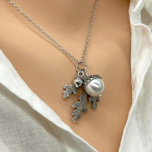 May include: A silver necklace with an acorn charm featuring a pearl and oak leaves.