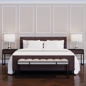 Puede incluir: Una cama con un cabecero blanco y ropa de cama blanca. La cama tiene un banco de madera oscura a juego al pie de la cama. Dos mesitas de noche con l&aacute;mparas est&aacute;n a cada lado de la cama. La habitaci&oacute;n tiene paredes blancas con molduras decorativas.