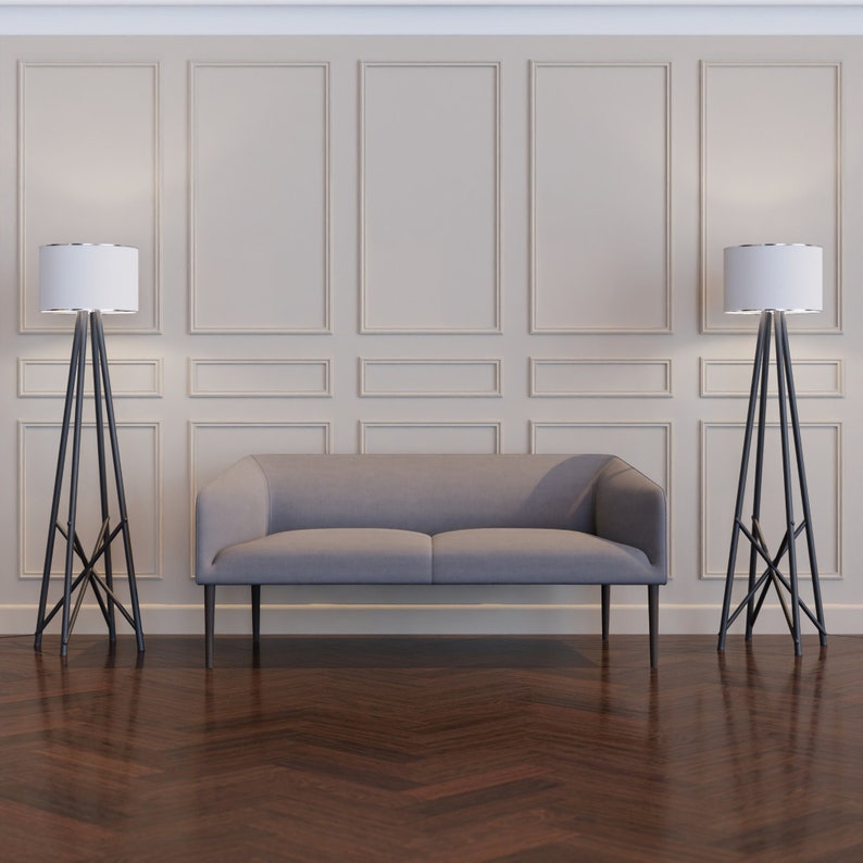 Puede incluir: Un sof&aacute; gris de tela con un marco de madera se encuentra frente a una pared con z&oacute;calos blancos. Dos l&aacute;mparas de pie negras con pantallas blancas se encuentran a cada lado del sof&aacute;.