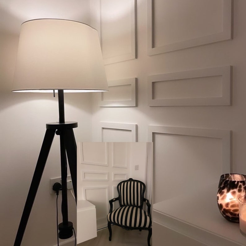 Puede incluir: Una l&aacute;mpara de pie negra con tr&iacute;pode y pantalla blanca ilumina una habitaci&oacute;n con paredes blancas y marcos de fotos blancos. Un sill&oacute;n de rayas blancas y negras se encuentra en la esquina de la habitaci&oacute;n.
