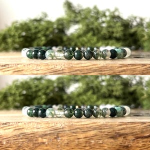 May include: A bracelet made of green and clear beads. The beads are round and vary in colour, with some solid green and others with a speckled pattern. The bracelet is displayed on a wooden surface.