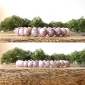 Puede incluir: Una pulsera de cuentas rosas con una mezcla de tonos rosas claros y oscuros. La pulsera est&aacute; hecha de cuentas redondas y se muestra sobre una superficie de madera con follaje verde en el fondo.