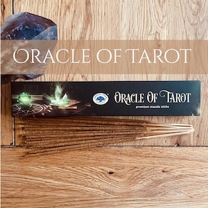 May include: A wooden surface displays a box of "Oracle of Tarot" premium masala sticks, with a crystal and the text "Oracle of Tarot" in white. The box is black with a green tree logo.
