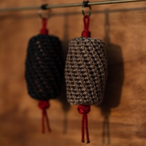 以下が含まれることがあります： 真鍮の棒に赤い房がついた、2つの編まれたロープ製のボトルストッパーがぶら下がっています。ストッパーは黒と茶色です。