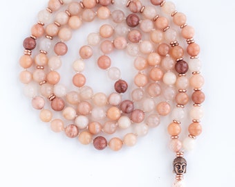 May include: A light pink and brown mala necklace with a small Buddha charm and a tassel. The necklace is made of natural stones and is approximately 108 beads long.