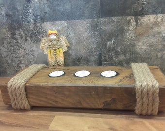May include: Rustic wooden candle holder with three candle wells, decorated with natural rope accents. The holder is made of reclaimed wood and has a natural, weathered finish.