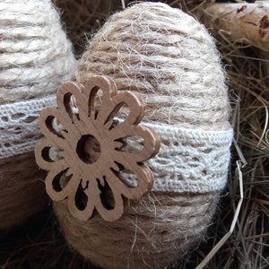 Op de afbeelding: Twee bruine paaseieren omwikkeld met touw, versierd met witte kant en een houten bloemuitsparing.