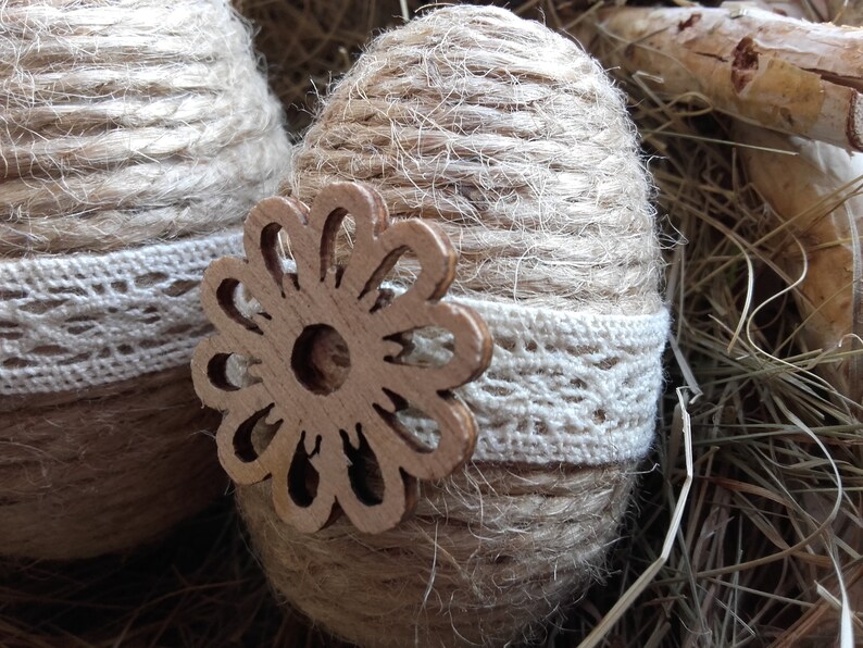 Op de afbeelding: Twee bruine paaseieren omwikkeld met touw, versierd met witte kant en een houten bloemuitsparing.