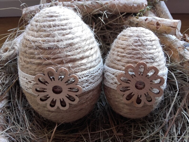 Op de afbeelding: Twee bruine paaseieren gewikkeld in touw en versierd met witte kant en een bruine houten bloemuitsparing.