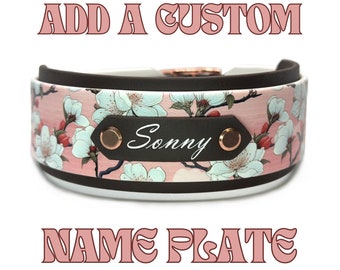 May include: A collar featuring a pink background with a white floral pattern and a dark brown central name plate with the name Sonny in white script, secured by two copper-colored rivets. The text ADD A CUSTOM NAME PLATE appears in pink.