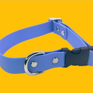 May include: A light blue dog collar with a silver-colored metal D-ring and buckle. The collar has a black plastic clasp and is secured with silver rivets. The background is a solid yellow.
