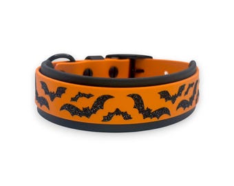 May include: A pet collar featuring a bright orange strap with a repeating pattern of black glittery bats. The collar includes a black buckle, a black D-ring for attachment, and a black inner lining, creating a high-contrast design for visibility.