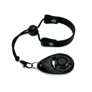 May include: Black dog training remote with a black leather strap and a black button. The remote has a small black button on the side.