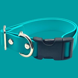 May include: A teal dog collar with a black plastic buckle and silver-colored metal hardware. The collar is made of a flexible material and is designed to be adjustable. The background is a solid teal color.