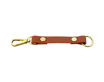 May include: A brown leather key chain with two gold metal snaps and a gold metal clip on one end and a gold metal ring on the other end.