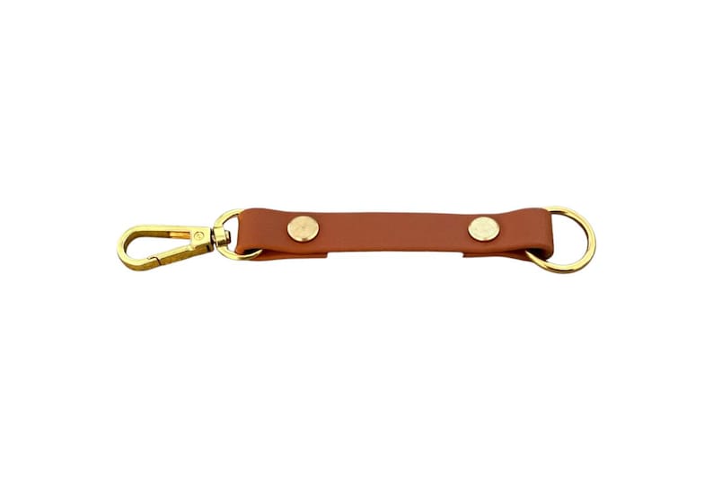 May include: A brown leather key chain with two gold metal snaps and a gold metal clip on one end and a gold metal ring on the other end.