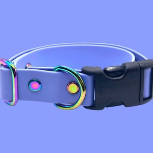 May include: A lavender dog collar with a black plastic buckle and iridescent metal hardware. The collar features a D-ring and rivets with a rainbow sheen. The background is a solid lavender color.