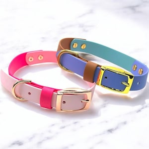 May include: Two colourful dog collars with gold buckles. One collar is pink and white, the other is blue, brown, and green.